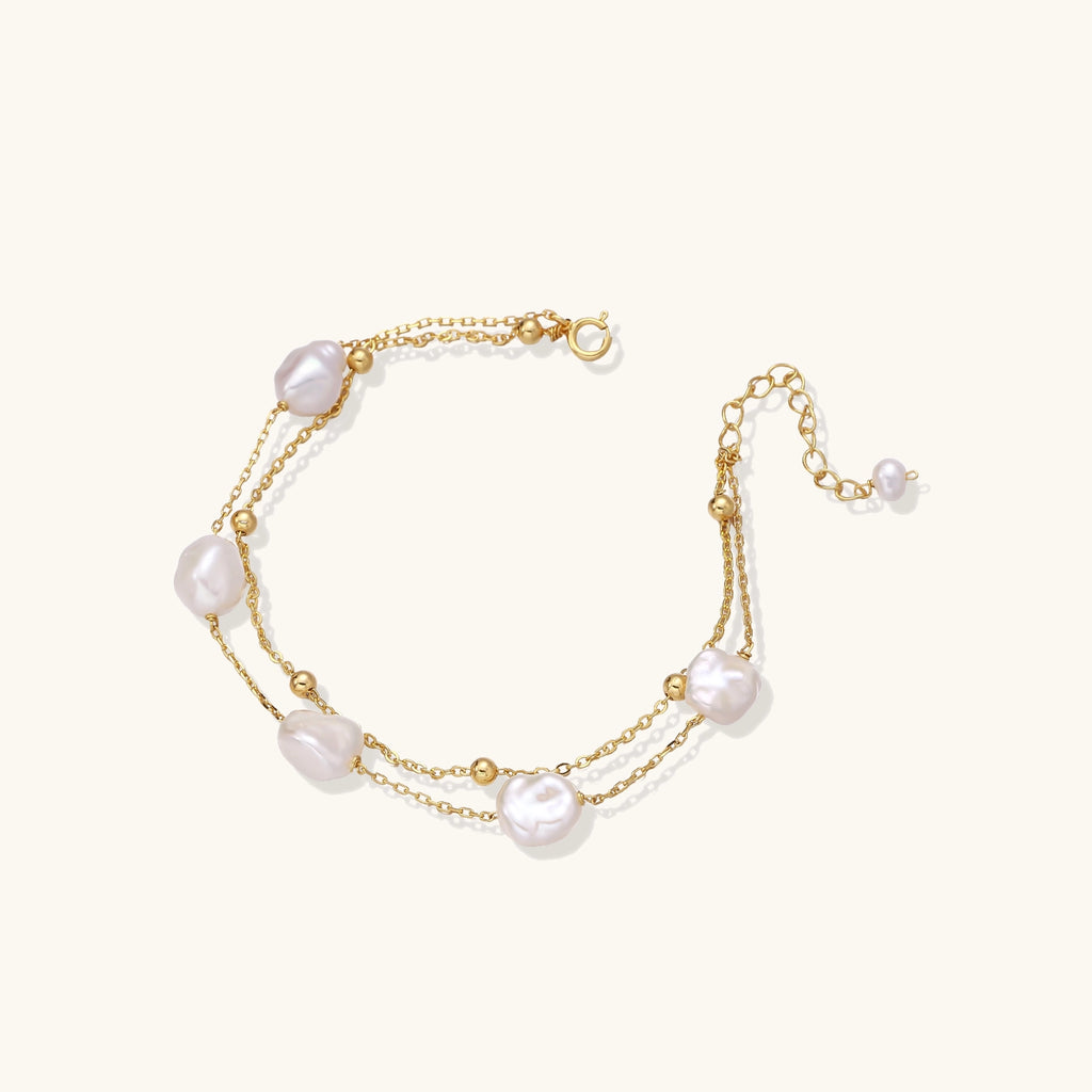 Delicate multi-layered gold-plated bracelet with irregular baroque pearls and freshwater pearls on cream background.
