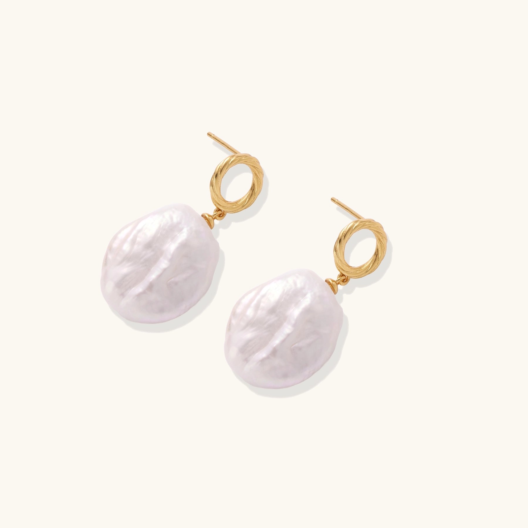 Gold-plated twisted stud earrings with large blush baroque pearls hanging elegantly on white background.