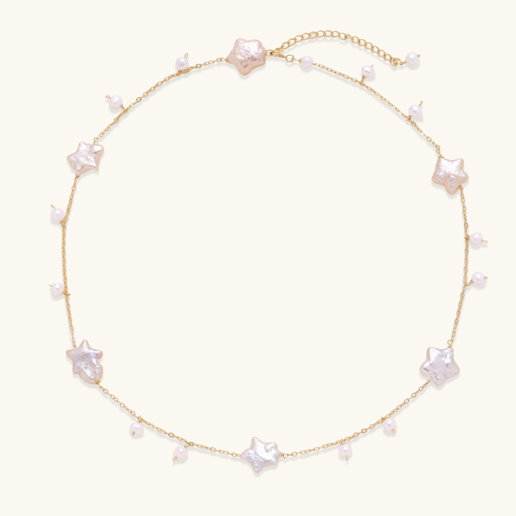 Delicate gold chain necklace with star-shaped baroque pearls and small freshwater pearls on cream background.