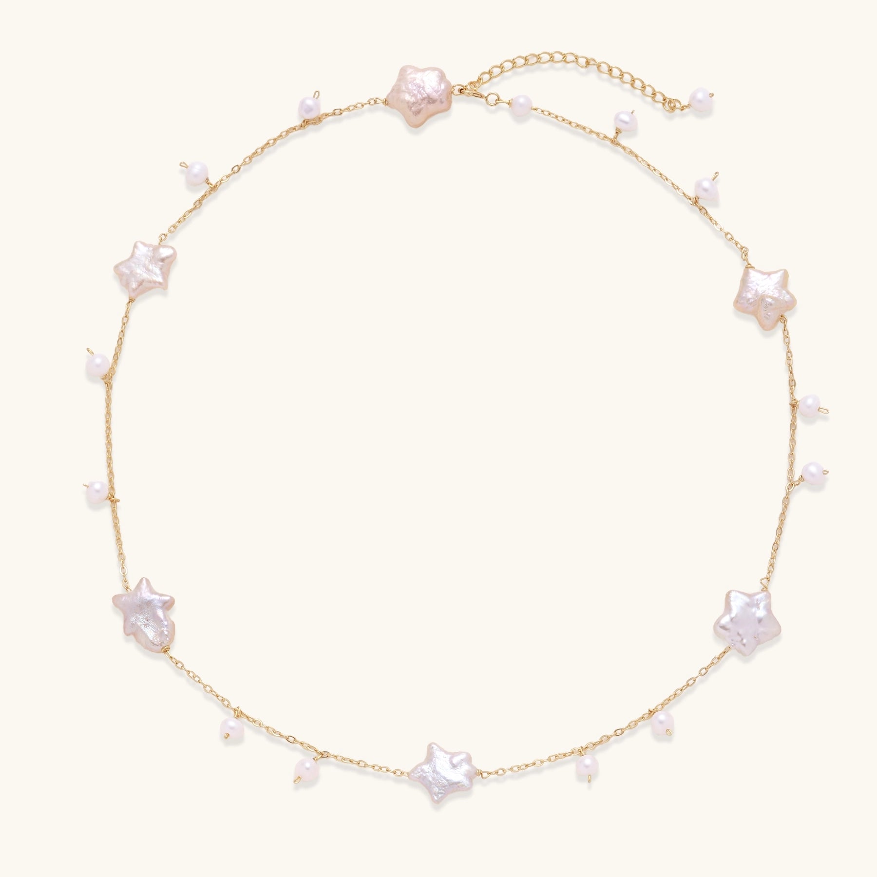 Delicate gold chain necklace with star-shaped baroque pearls and small freshwater pearls on cream background.