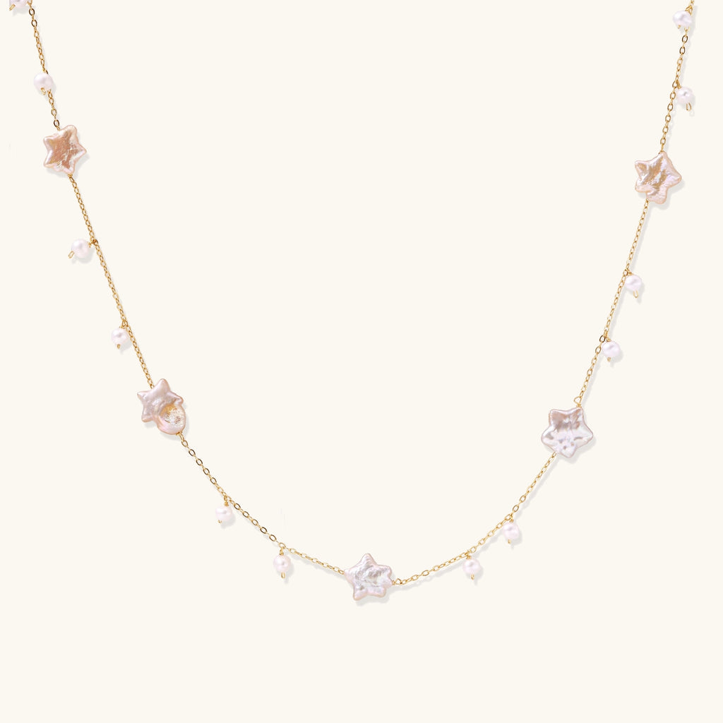 Delicate gold chain necklace with star-shaped baroque pearls and small freshwater pearls on cream background.