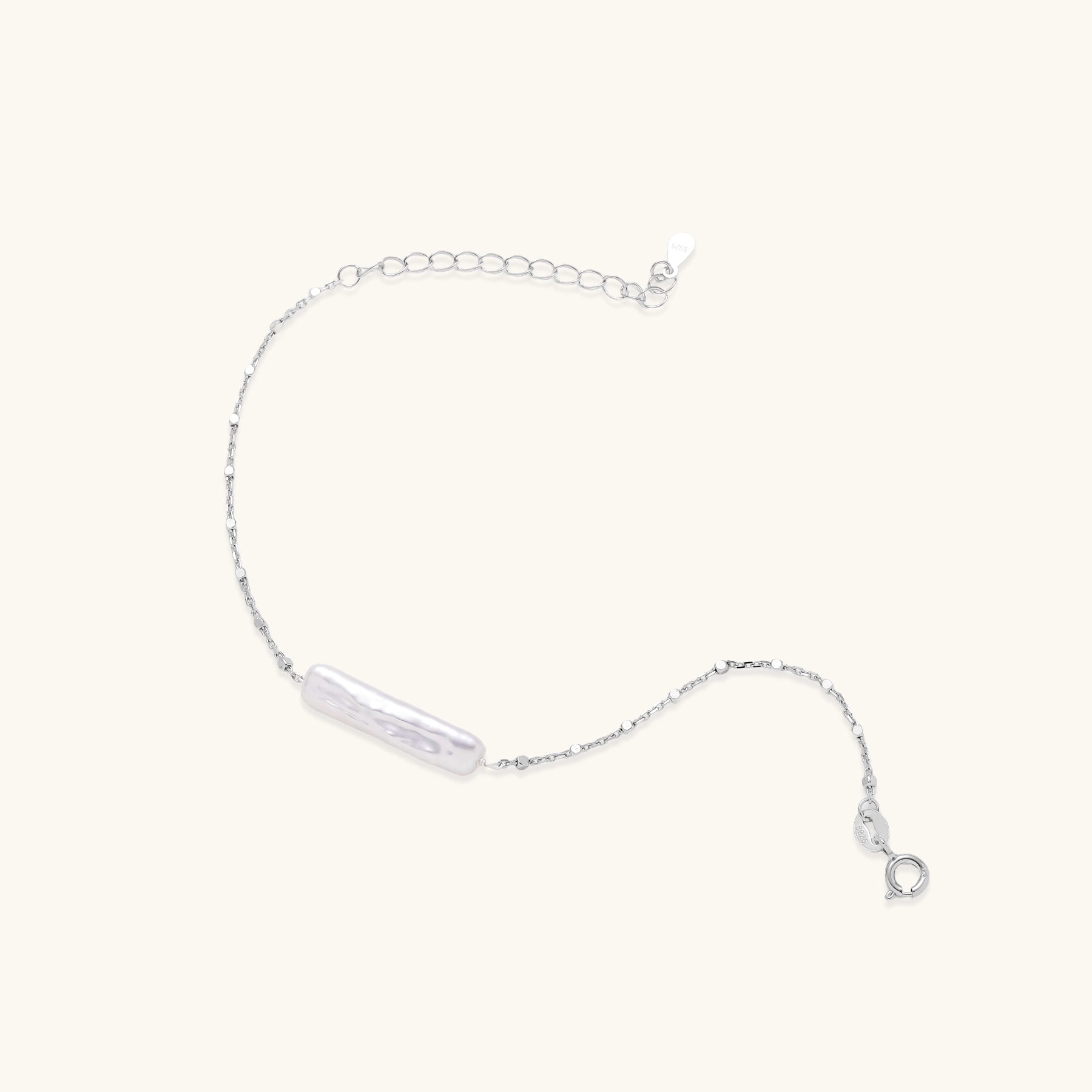 Delicate sterling silver chain bracelet with an organic white baroque pearl centerpiece on neutral background