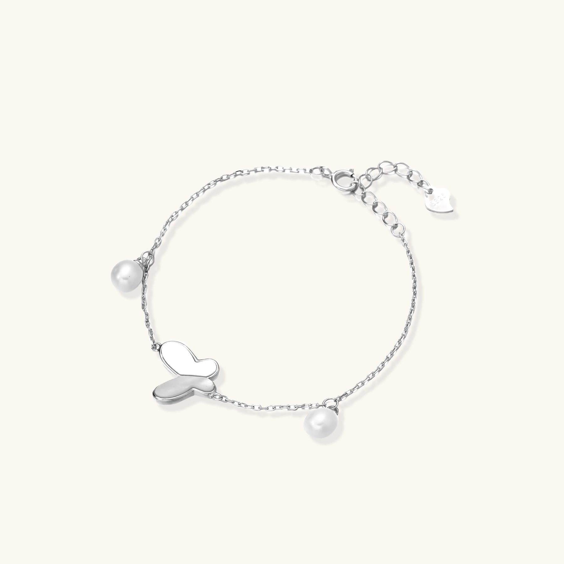 Dainty sterling silver chain bracelet with heart charm and freshwater pearl dangles on white background.