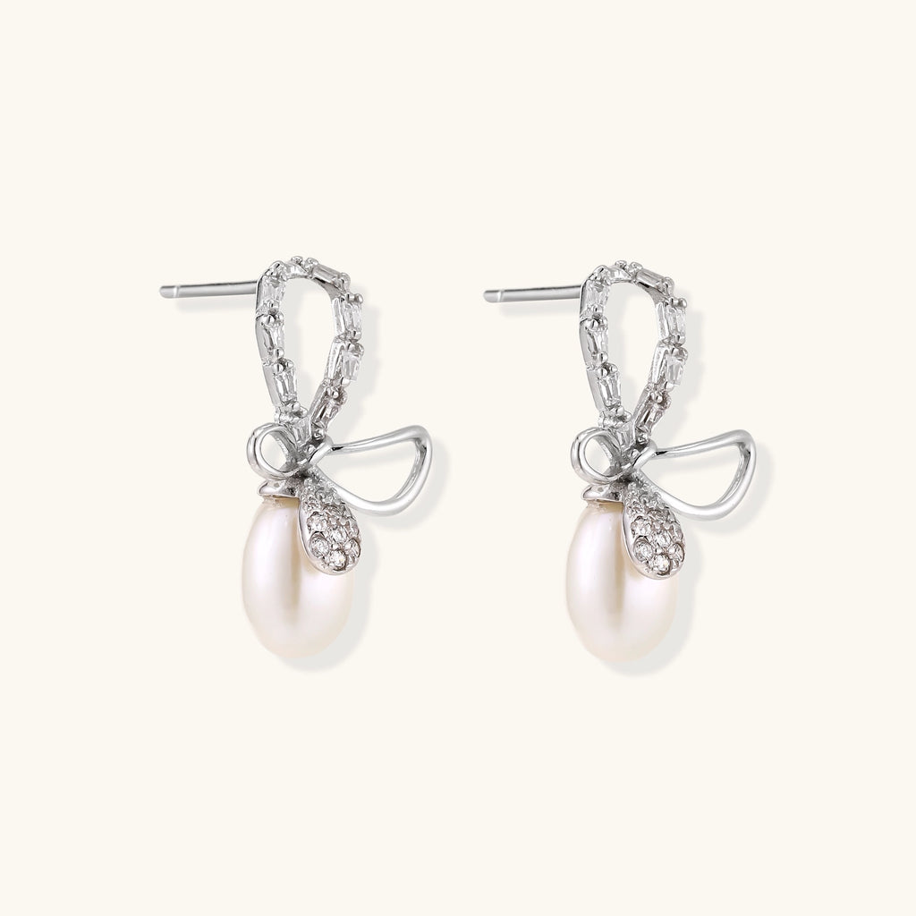Sterling silver stud earrings with baguette crystal bow design and freshwater pearl drops on white background