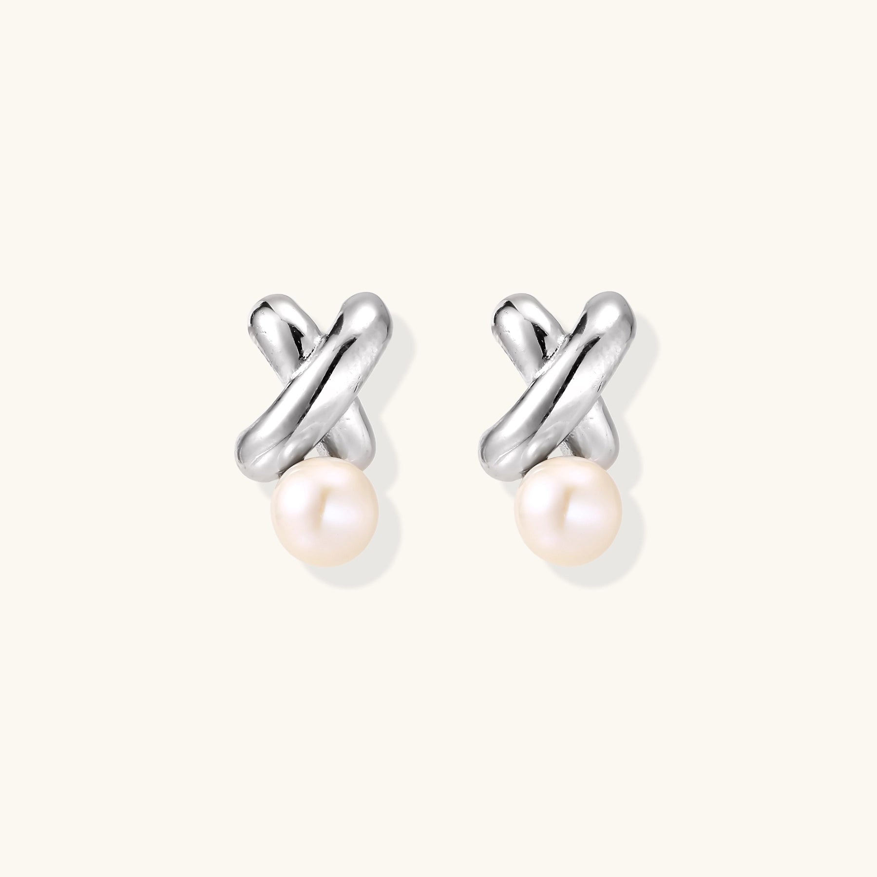 Sterling silver twisted stud earrings with round freshwater pearls on cream background, showing polished finish