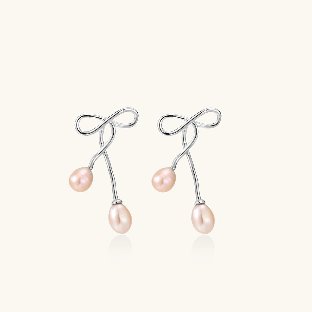 Delicate sterling silver wire earrings with organic bow shapes and two pink freshwater pearls on white background