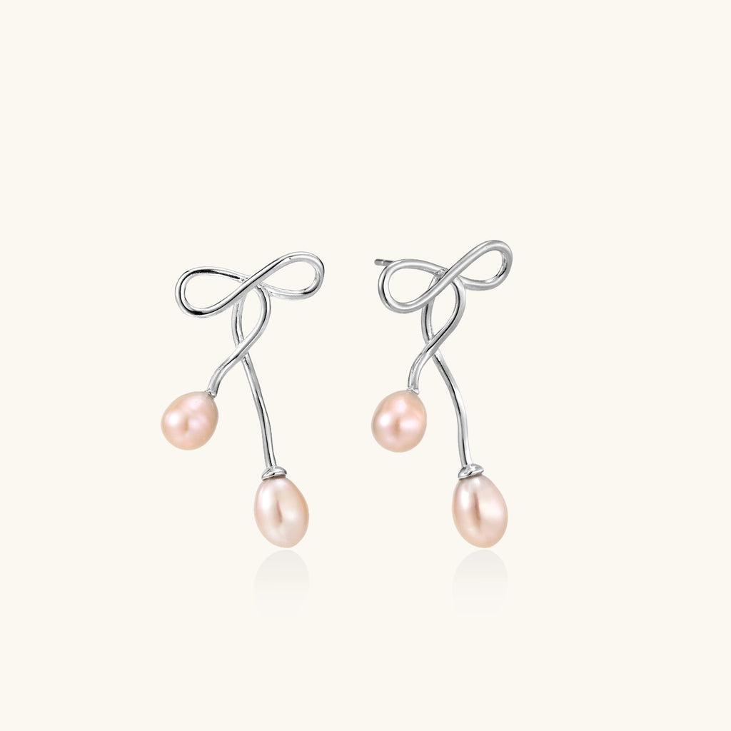 Delicate sterling silver wire earrings with organic bow shapes and two pink freshwater pearls on white background