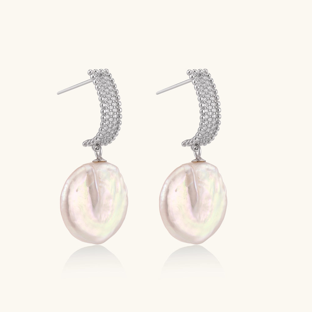 Sterling silver huggie earrings with lustrous baroque pearls displaying iridescent pink and cream tones on white background.