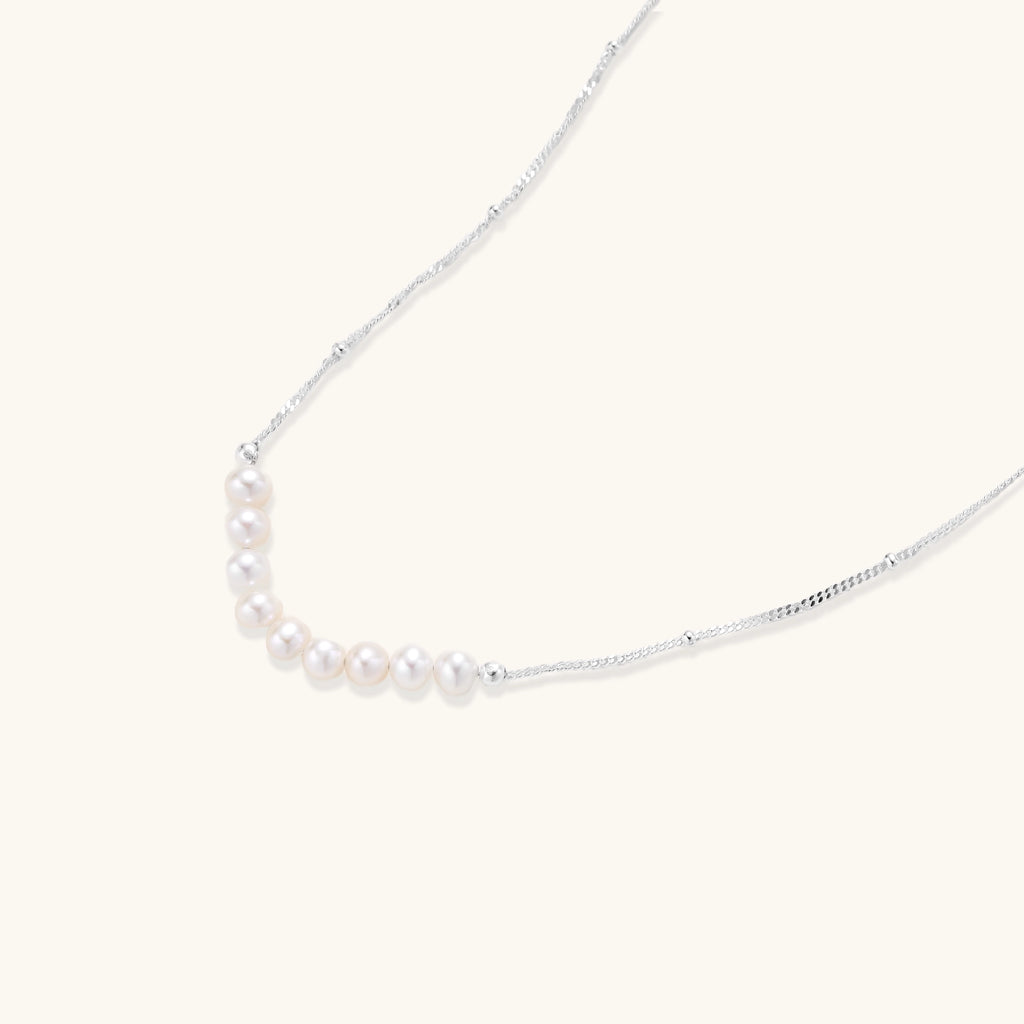 Delicate sterling silver chain with small white freshwater pearls arranged asymmetrically on white background.
