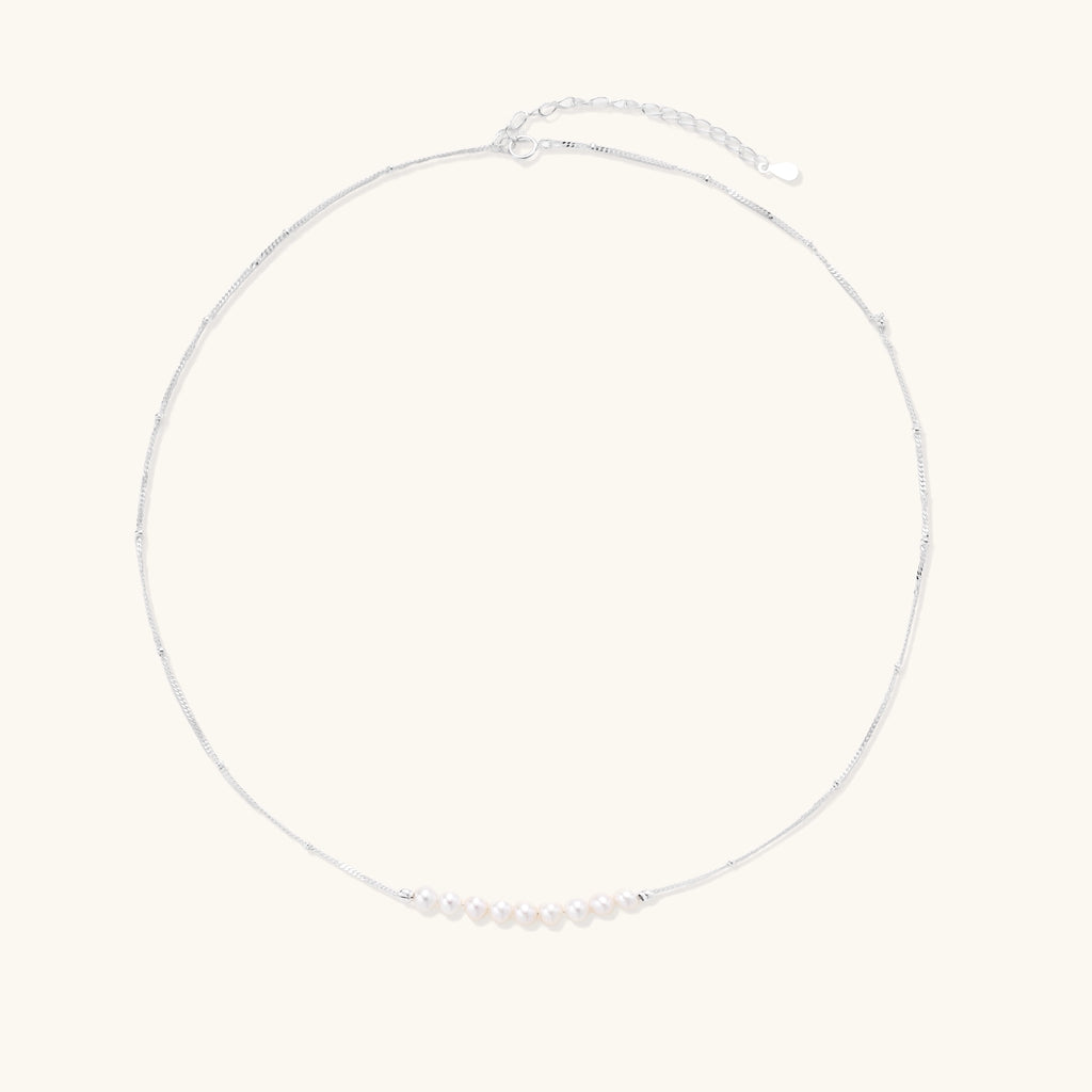 Delicate sterling silver chain with small white freshwater pearls arranged asymmetrically on white background.