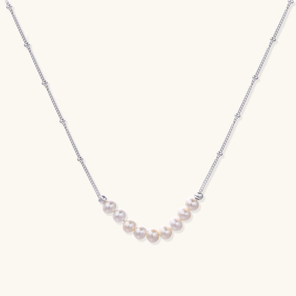 Delicate sterling silver chain with small white freshwater pearls arranged asymmetrically on white background.
