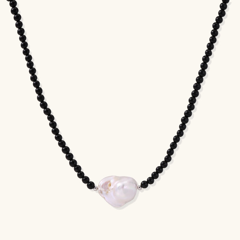 Elegant necklace with black agate beads and iridescent baroque freshwater pearl centerpiece on white background.