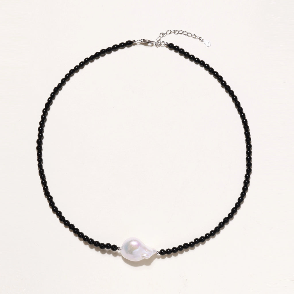 Elegant necklace with black agate beads and iridescent baroque freshwater pearl centerpiece on white background.