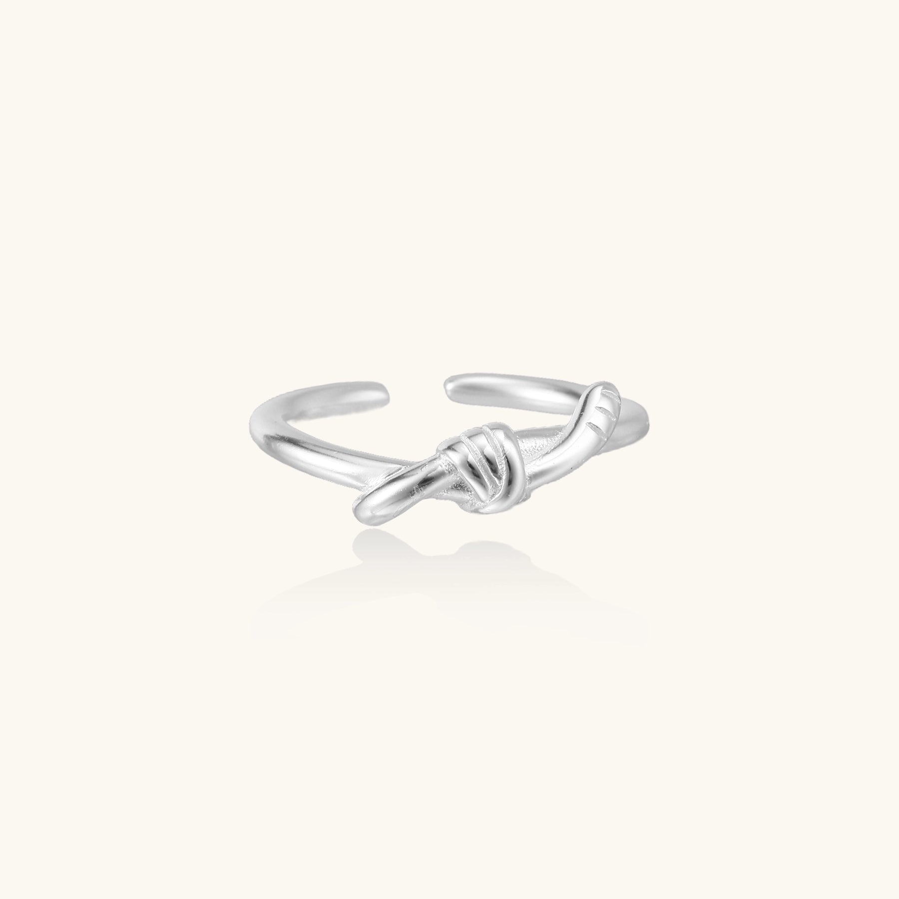 Delicate sterling silver ring with geometric knot design on white background, showcasing adjustable open band.