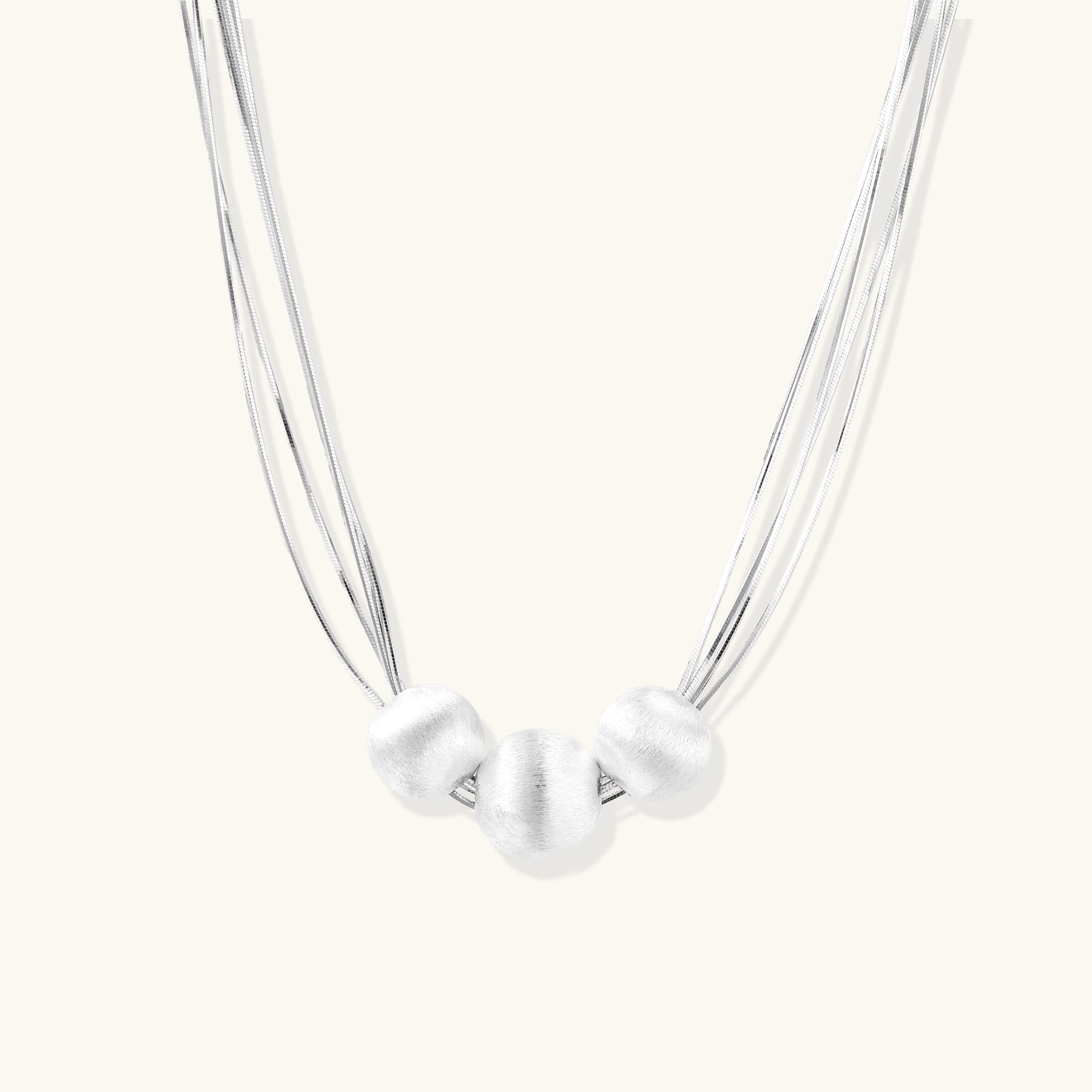 Multi-strand sterling silver necklace with three polished round beads clustered at center on white background.