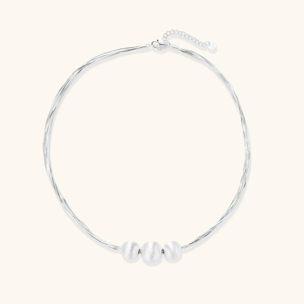 Multi-strand sterling silver necklace with three polished round beads clustered at center on white background.