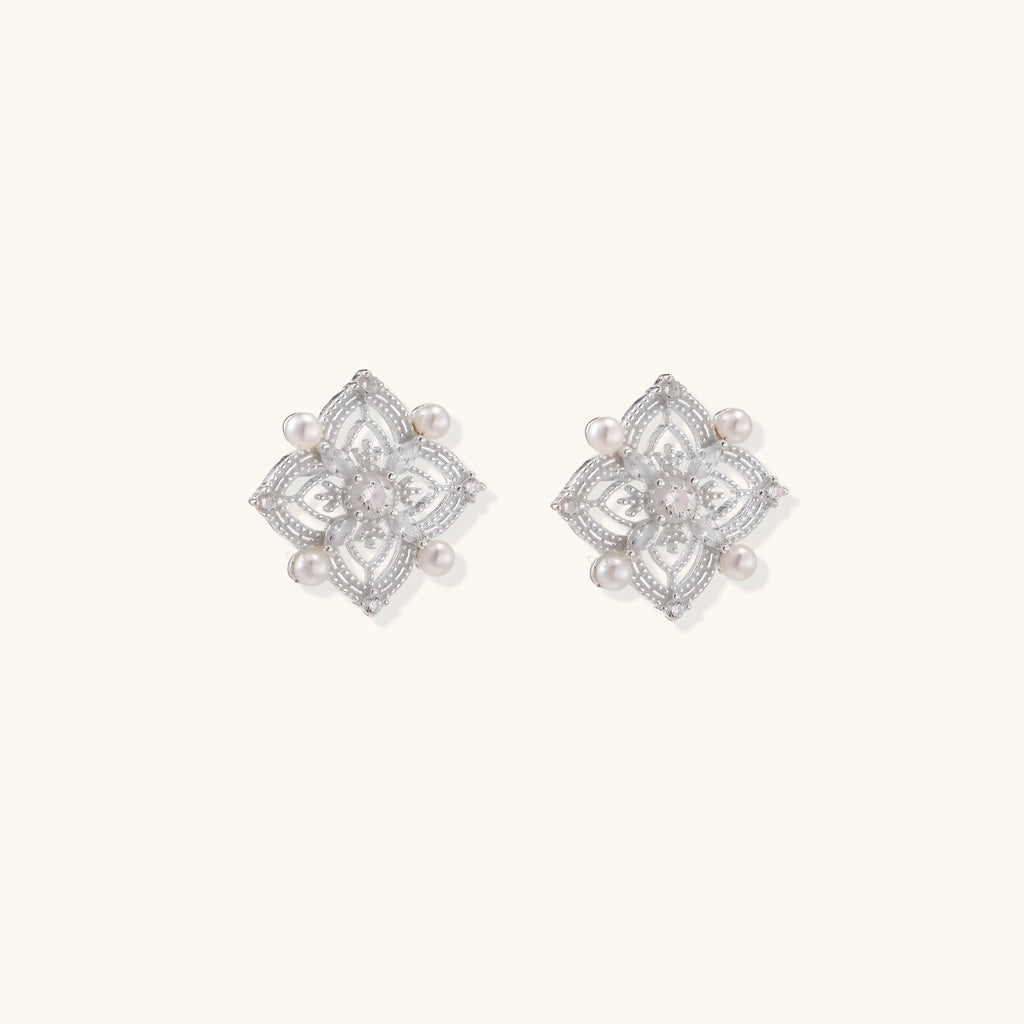 Detailed view of sterling silver stud earrings with geometric filigree design and small freshwater pearls on white background.