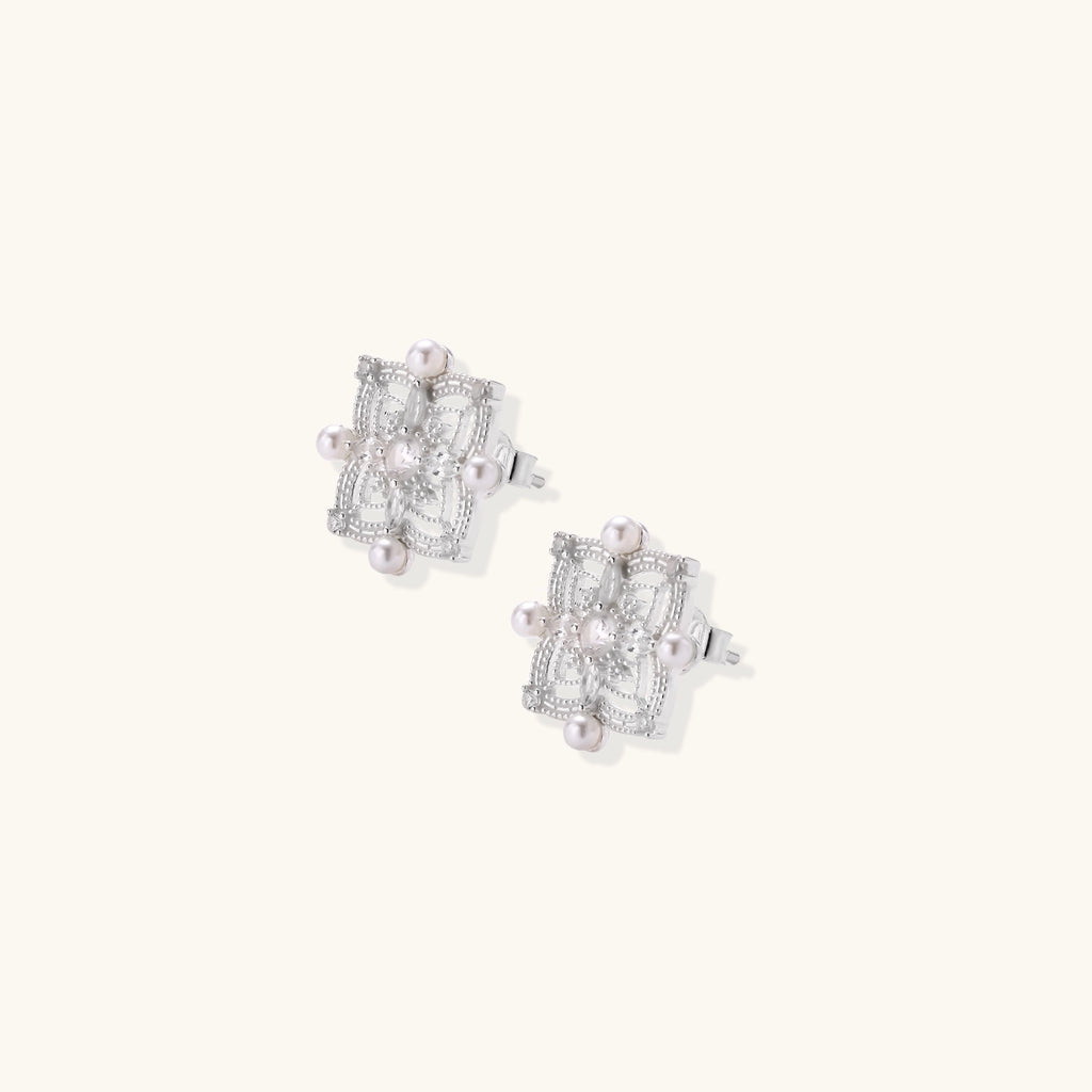 Detailed view of sterling silver stud earrings with geometric filigree design and small freshwater pearls on white background.