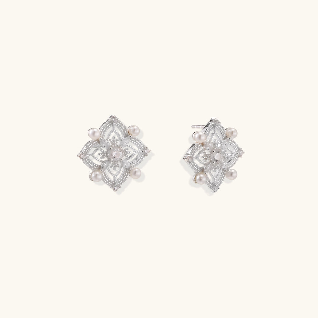 Detailed view of sterling silver stud earrings with geometric filigree design and small freshwater pearls on white background.