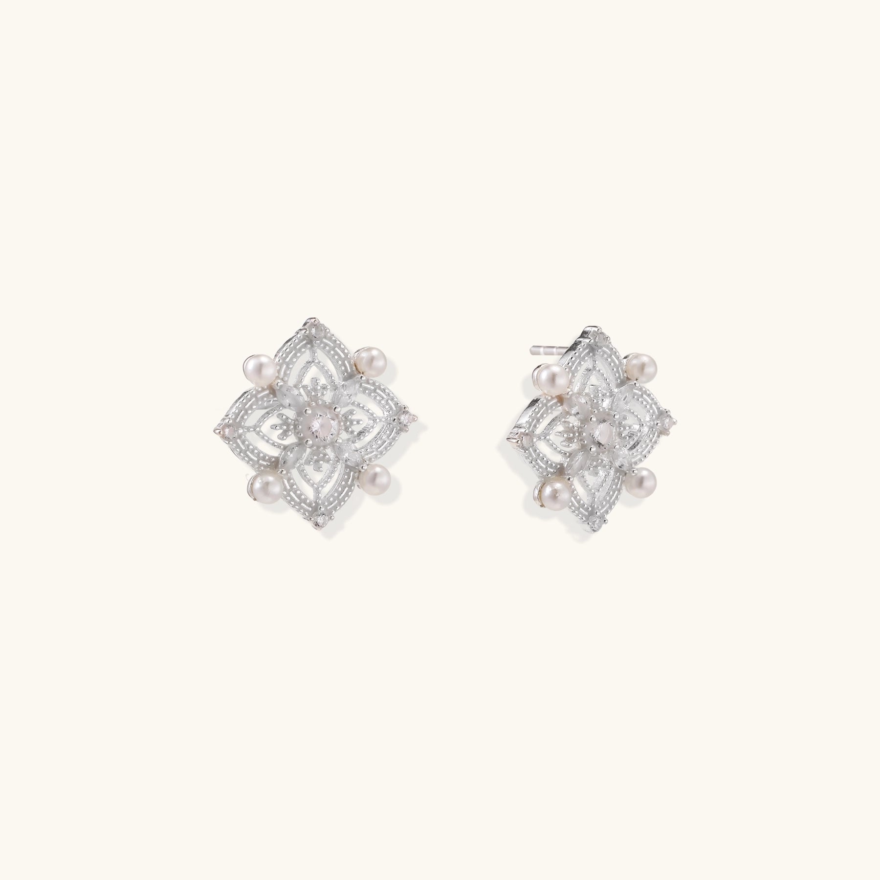 Detailed view of sterling silver stud earrings with geometric filigree design and small freshwater pearls on white background.