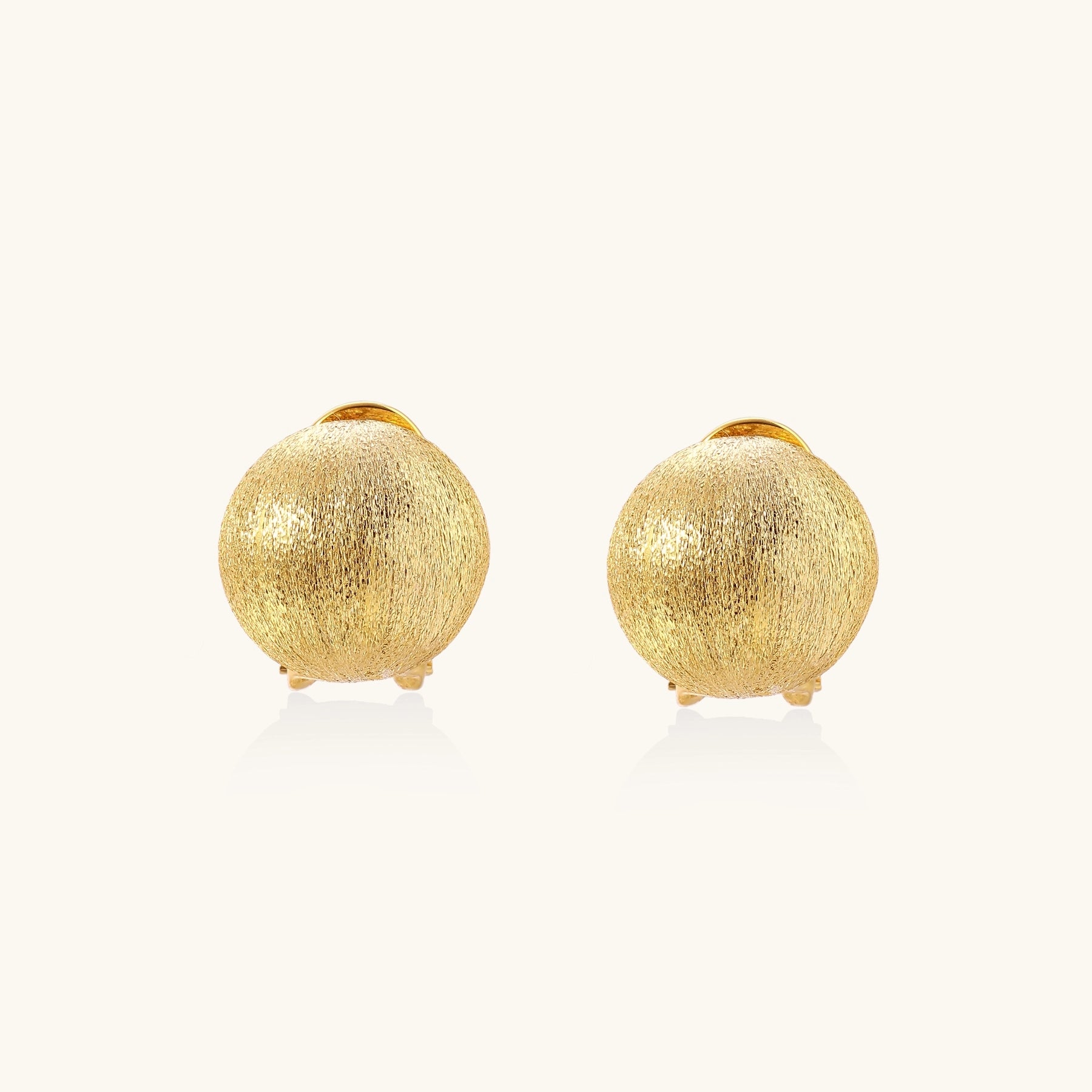 Close-up of textured gold-plated sterling silver dome clip-on earrings with brushed finish on white background.