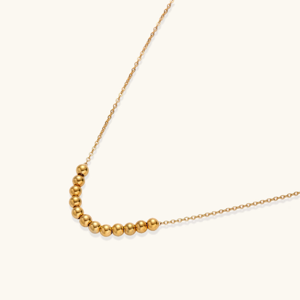 Delicate gold-plated chain necklace featuring clustered spherical beads arranged in elegant curve against white background.