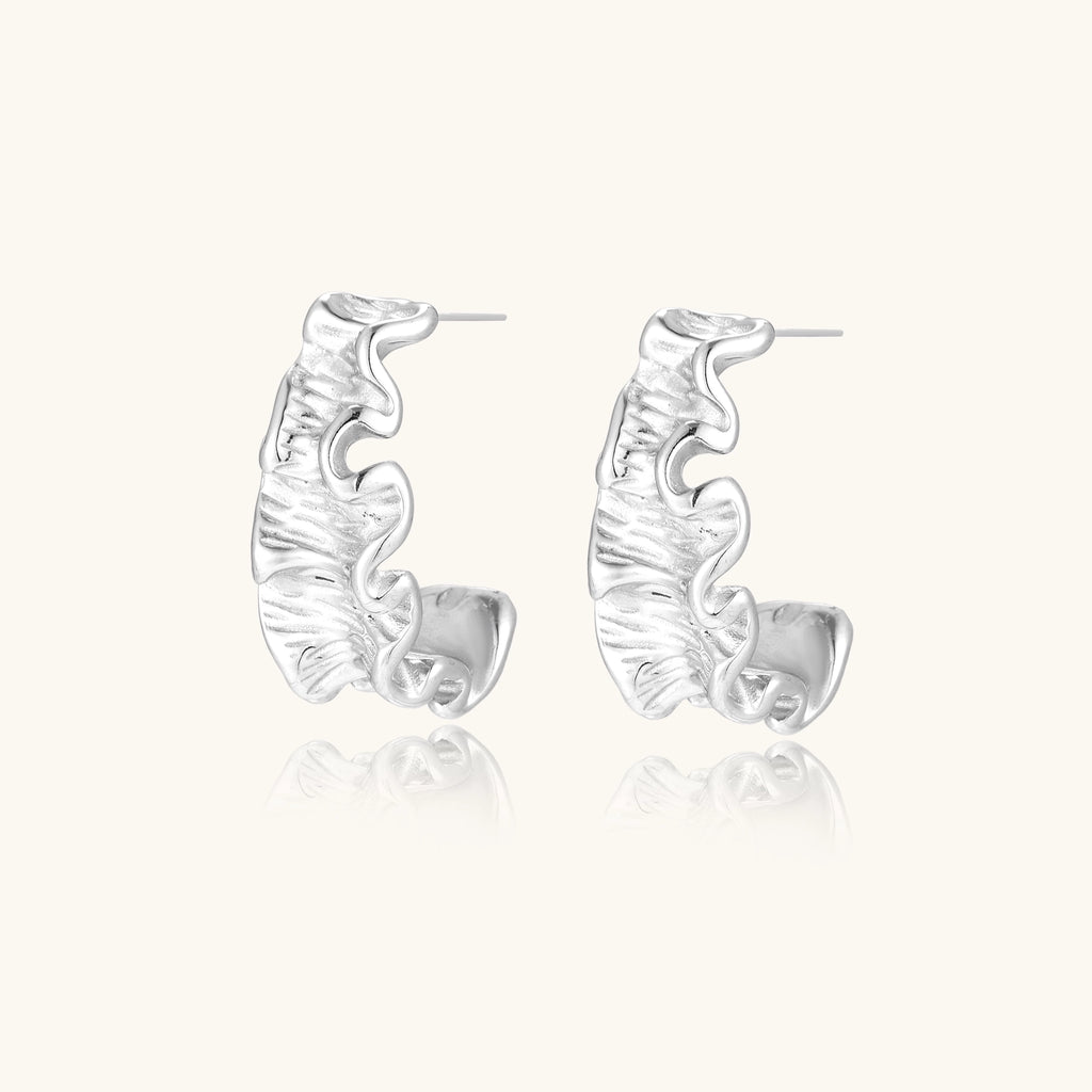 Textured gold-plated hoop earrings with flowing ripple design displayed on clean white background.