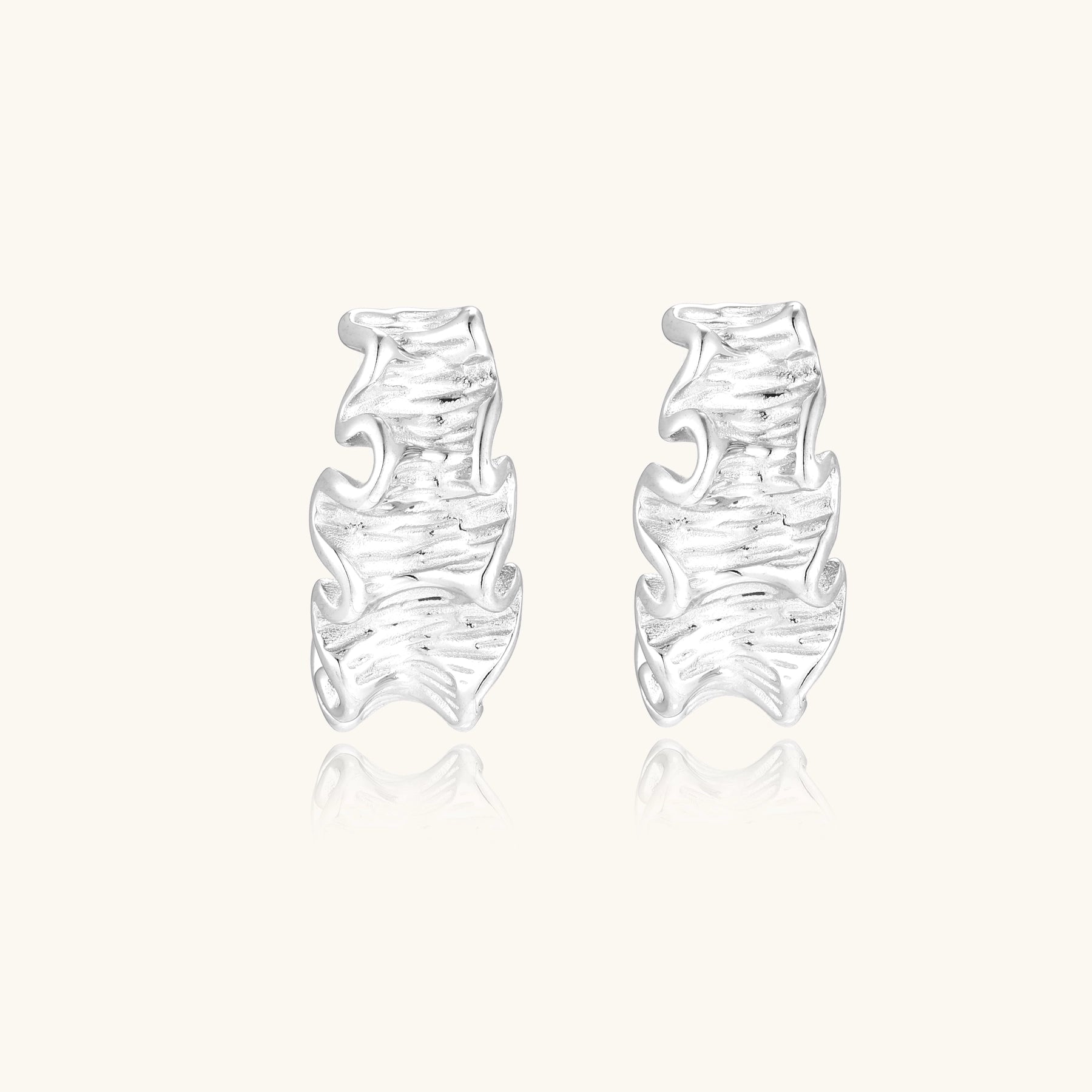 Textured gold-plated hoop earrings with flowing ripple design displayed on clean white background.