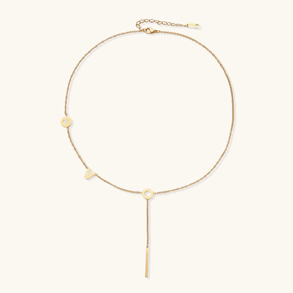 Gold-plated lariat necklace spelling LOVE with letter charms and vertical bar pendant on white background.