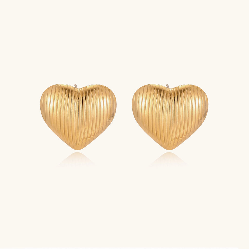 Close-up of ridged heart-shaped gold-plated stud earrings with textured surface pattern on cream background.