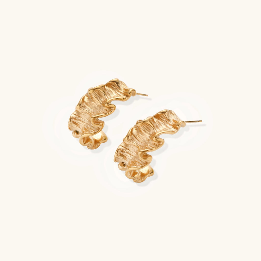 Textured gold-plated hoop earrings with wavy sculptural ridges displayed against a neutral background.