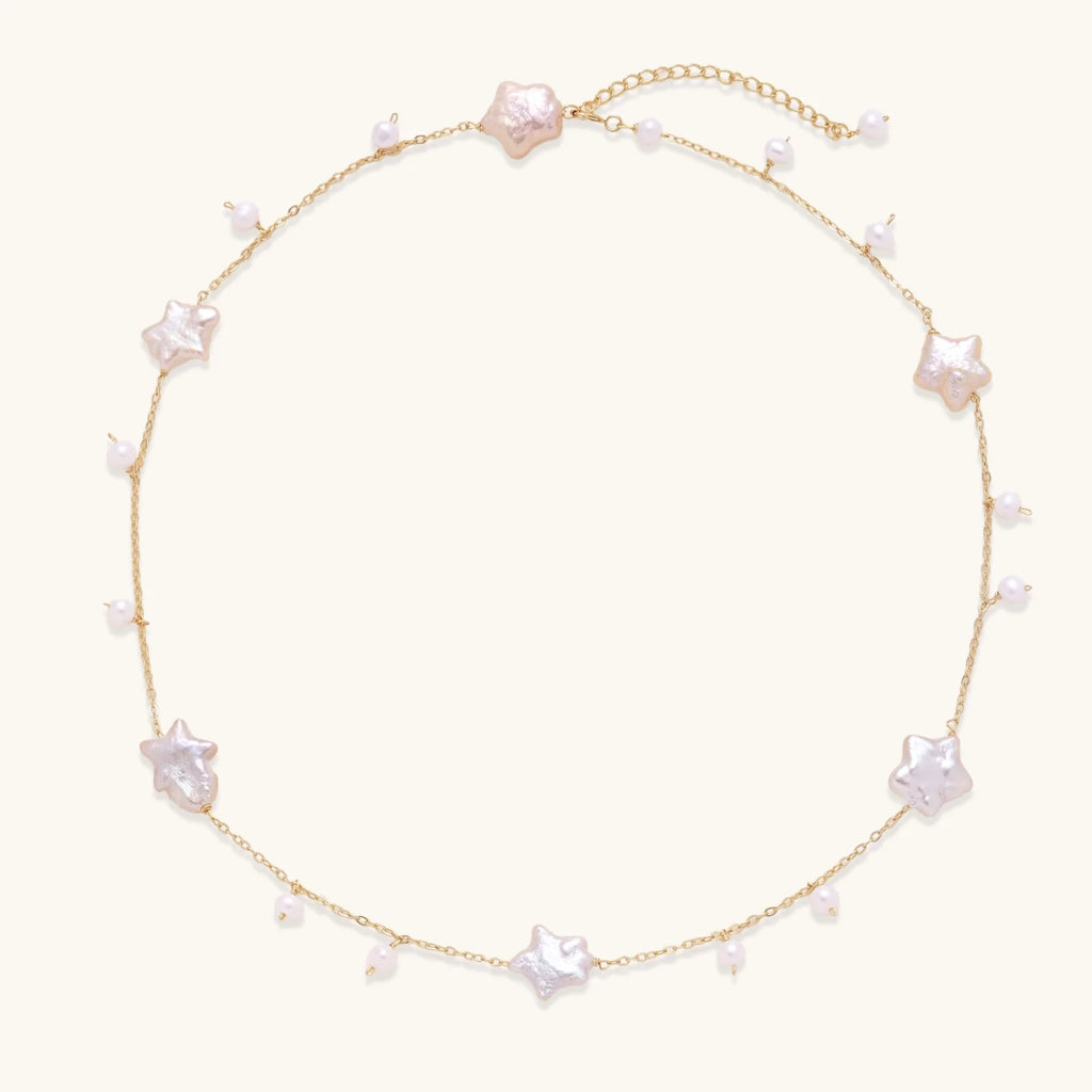 Gold vermeil chain with iridescent star-shaped baroque pearls and small round freshwater pearl drops on cream background.