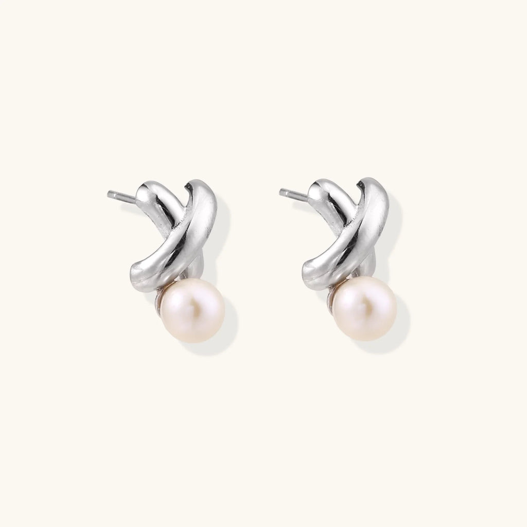 Rhodium-plated silver earrings with twisted X design and freshwater pearl drops on beige background