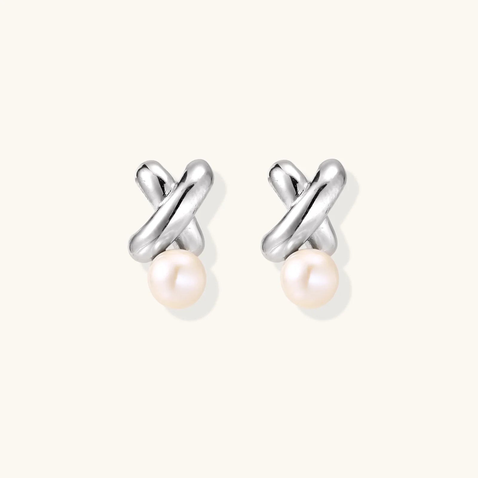 Rhodium-plated silver earrings with twisted X design and freshwater pearl drops on beige background