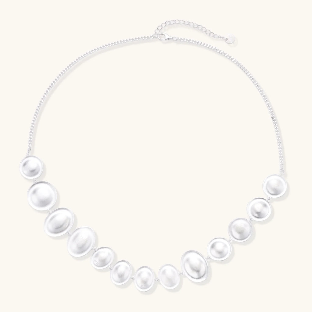 Graduated pearl-finish silver discs forming an organic bubble bib necklace on delicate chain against cream background.
